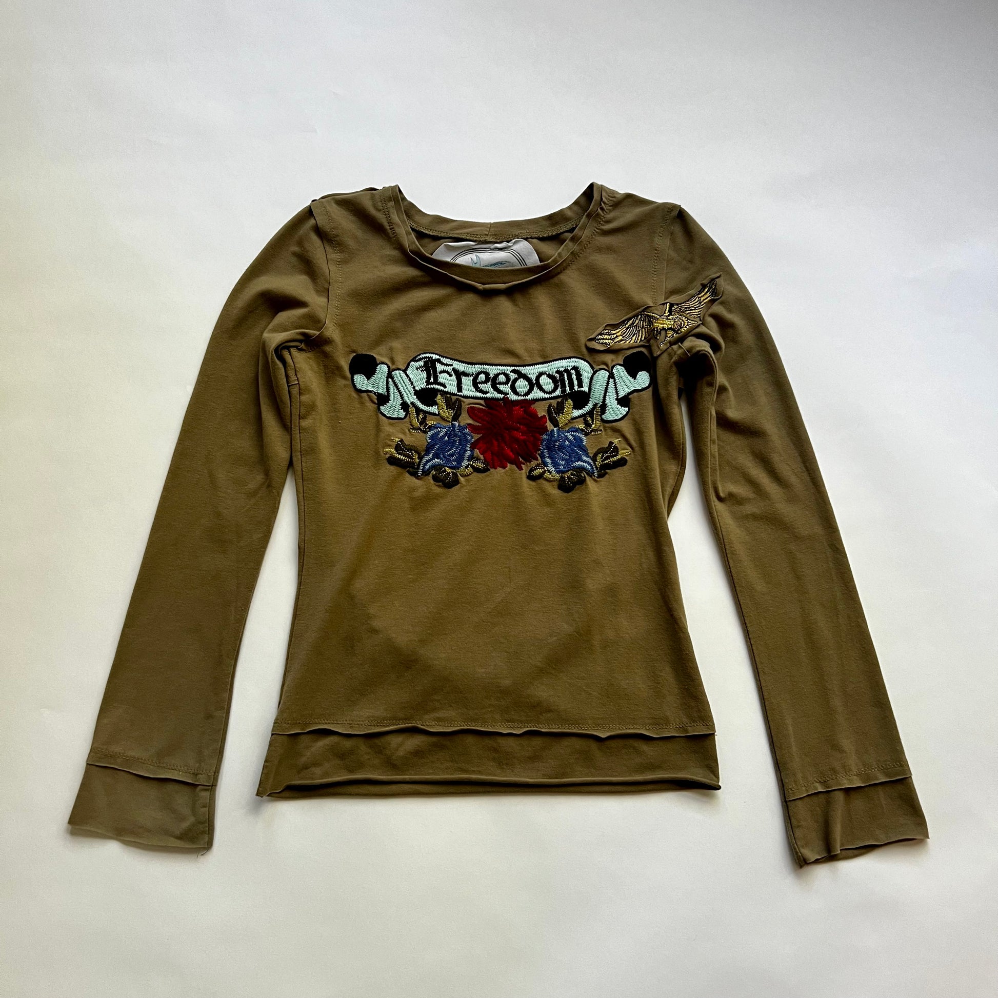 This is a long sleeve top with multicolored embroidery graphic design. The design says 'freedom' on it.  Crewneck with raw edges. 